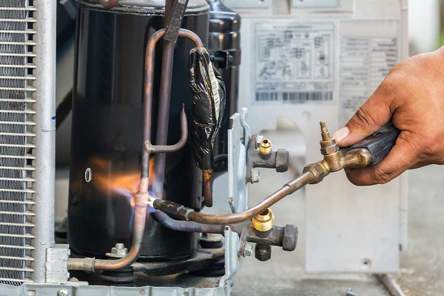 Technician using a torch during HVAC repair on an AC unit